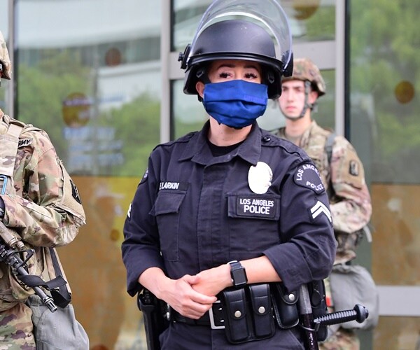 a police officer in full riot gear and helmet stands on the street in a mask