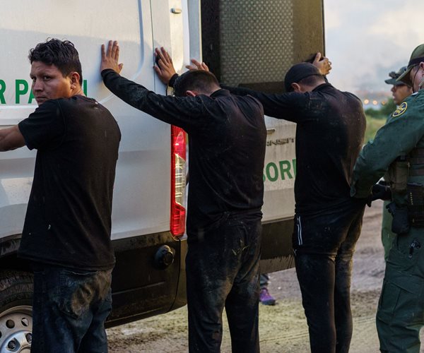 migrants stand facing border patrol van