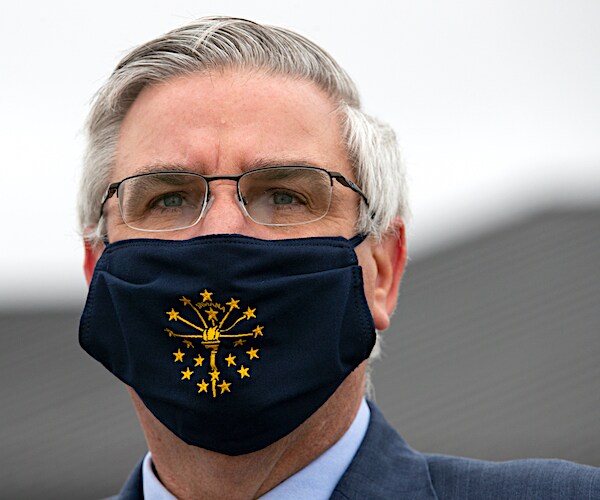 eric holcomb wears a face masks as he faces the media