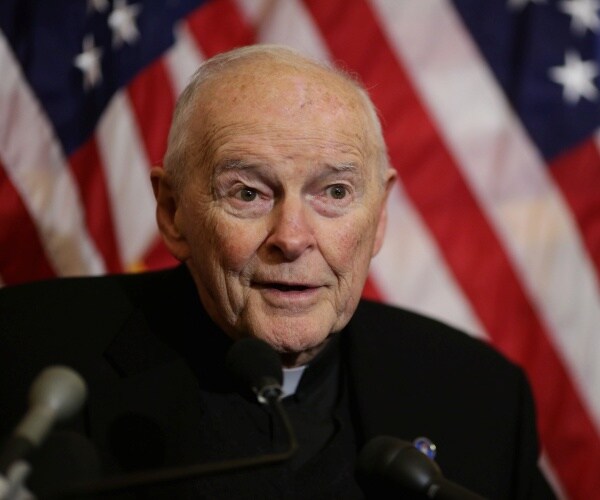 mccarrick in a black coat in front of the us flag