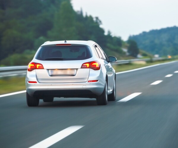 silver car driving on the highway with mountains on the side