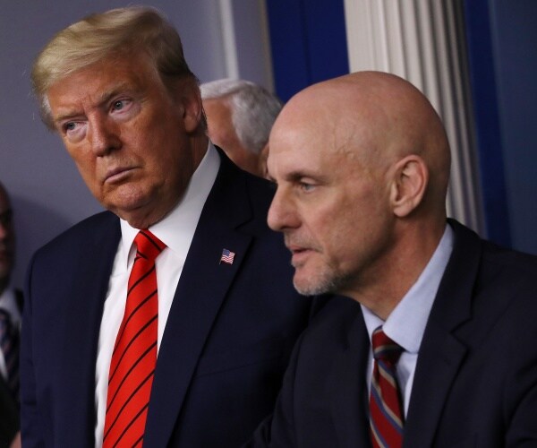trump in a suit and red striped tie looks on as hahn speaks to the press 