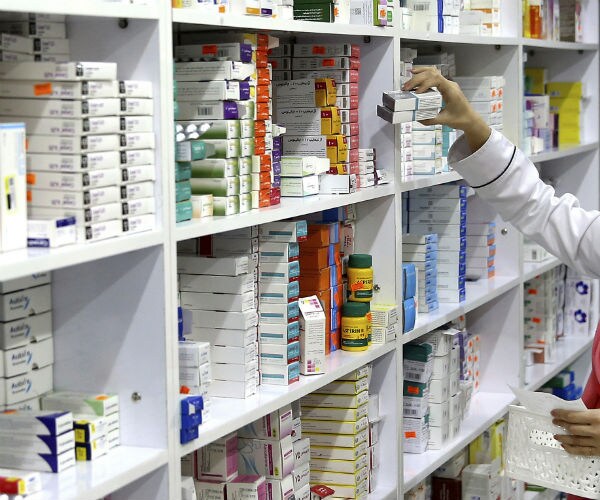 a drugstore employee reaches for medicine from a shelf