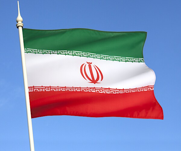 an iranian flag on a pole waves against a bright blue sky