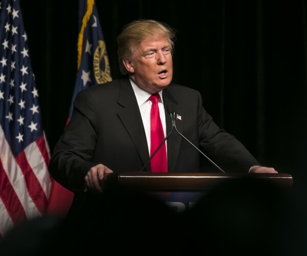 trump speaking in front of podium, american flag in back