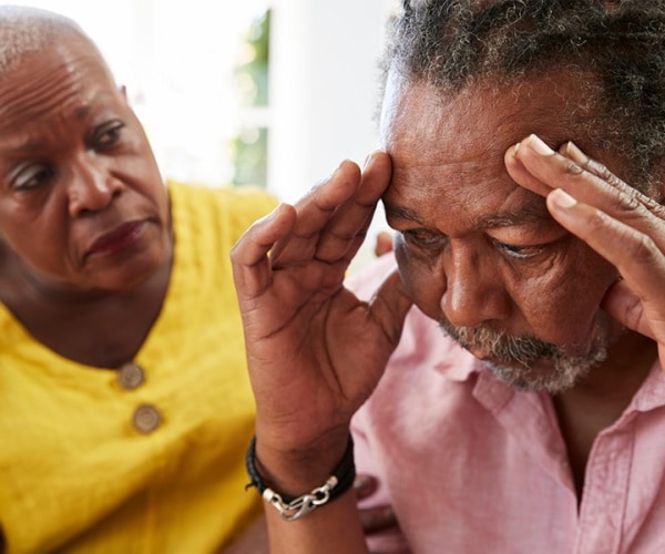 concerned woman looking at an upset man with head in hands