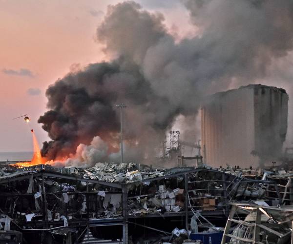 scene of blast in beirut with a helicopter dropping water on a fire