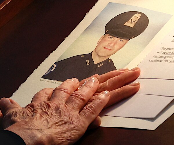 capitol police officer brian sicknick is shown on a memorial with an older woman's hands resting on the page