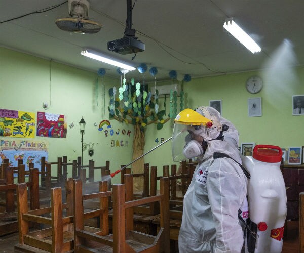 a health worker wearing protective gear disinfects a classroom