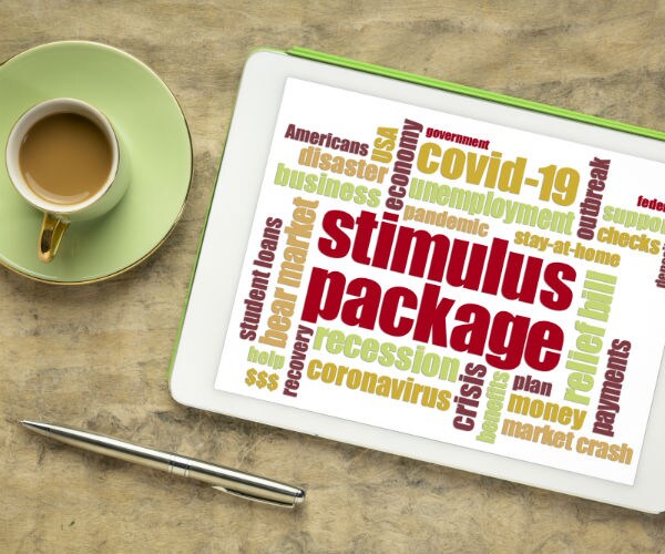 a cup of coffee sits on a green saucer with a silver pen and tablet with covid-19 and stimulus package shown