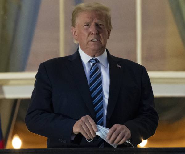 trump holds mask as he looks out over the balcony