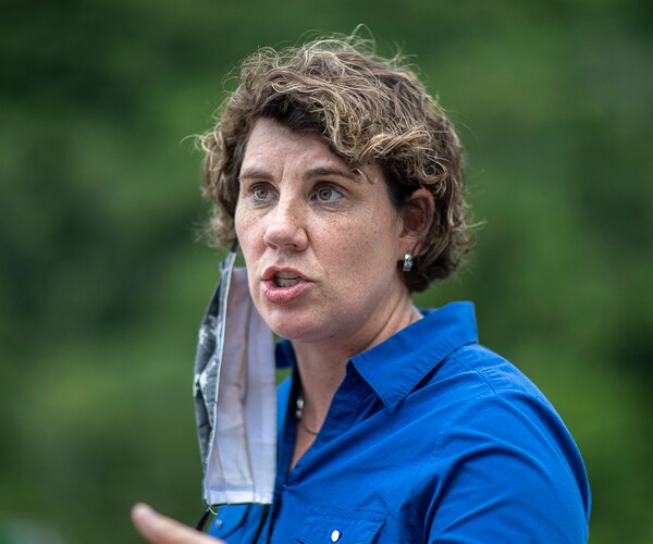 senate candidate amy mcgrath speaks with a face mask hanging off one ear