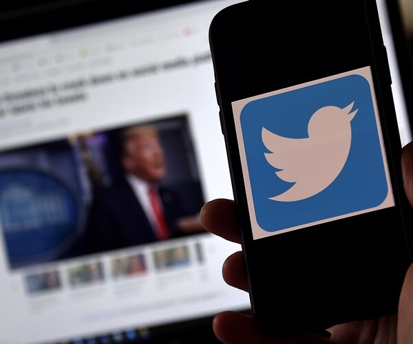 a twitter screen next to president trump on a monitor