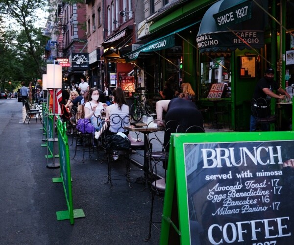 people sit at outdoor tables with some wearing masks and a brunch menu is seen