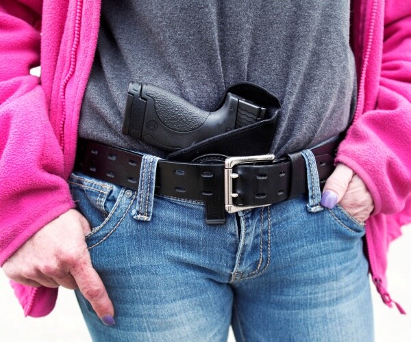 woman with a gun wearing jeans and a pink jacket