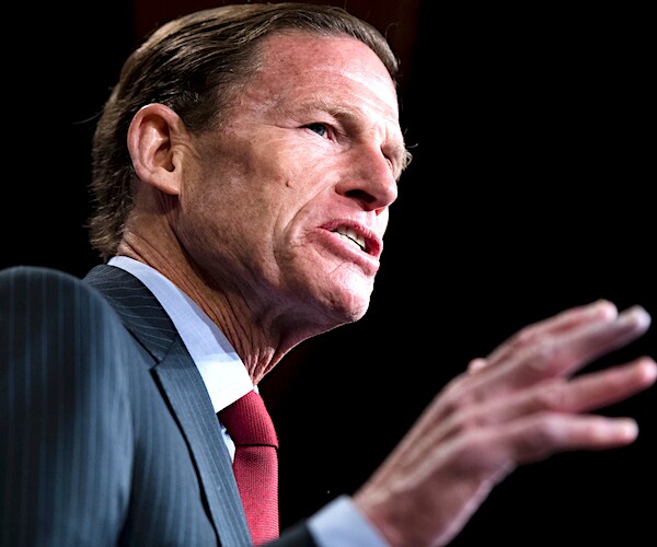 richard blumenthal gestures as he speaks on a dark stage