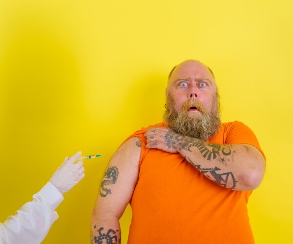 large man with tattoos looking fearful as a healthcare worker comes closer to his arm with syringe
