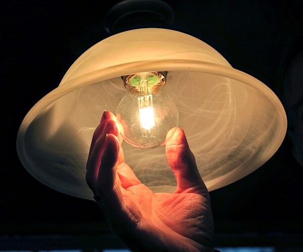 a man reaches up to change an incandescent light bulb