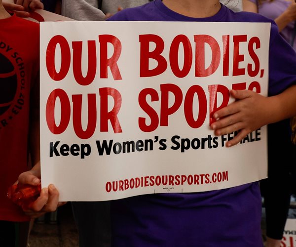 hands hold a sign that reads: our bodies our sports