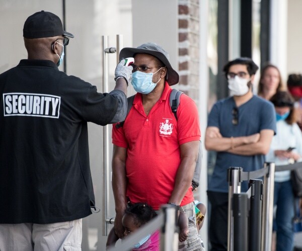man checks temperature of customers wearing face masks