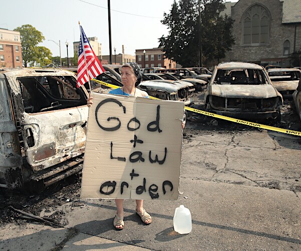 a woman stands in a car dealership lot burned by kenosha arsonists and rioters
