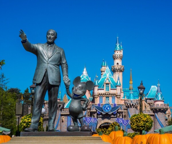 statue of walt disney holding mickey mouse in front of castle
