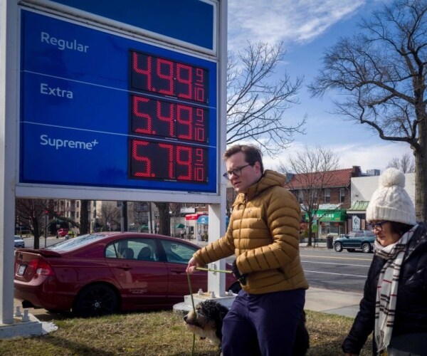 eople walk past a sign showing gas prices outside a gas station in washington dc