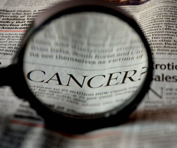 The word Cancer in a headline in a newspaper under a magnifying glass