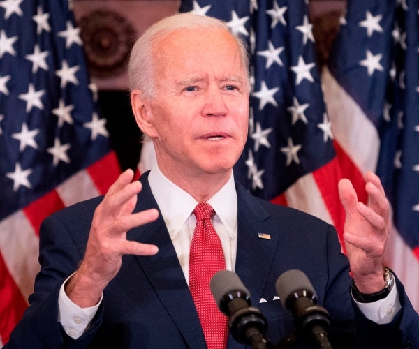biden in front of american flags and wearing a navy blue suit and red tie