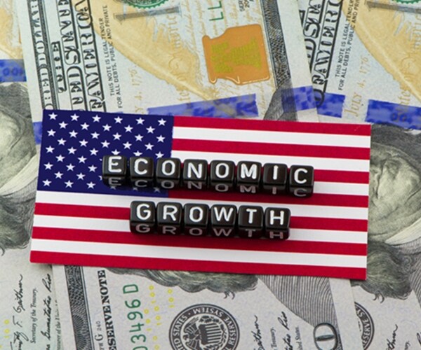 economic growth spelled in capital white letters on black blocks atop american flag and three one hundred dollar bills