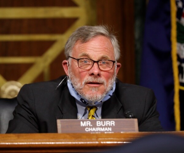 richard burr sitting and speaking at a hearing wearing a suit and blue shirt and yellow tie