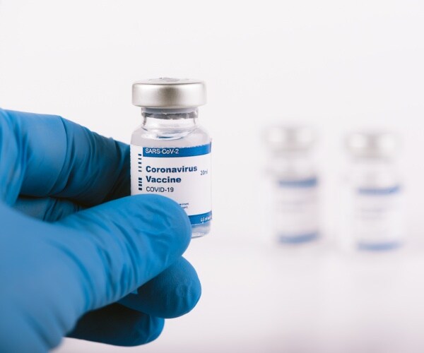 gloved hand holding a COVID vaccine vial with two more in the background