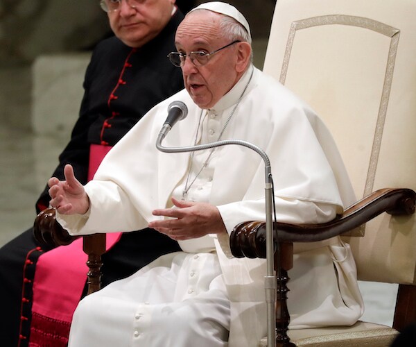 pope francis sits and speaks into a mic