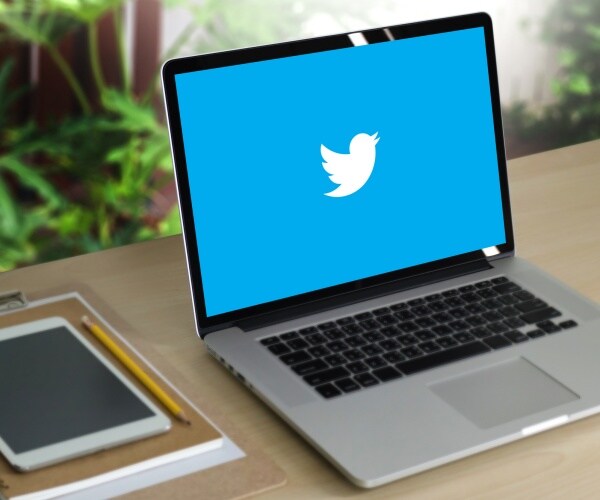 twitter logo shown on a laptop sitting on a wood desk
