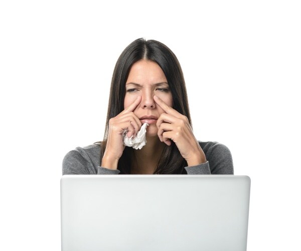 woman holding a tissue and area on either side of nose with pain
