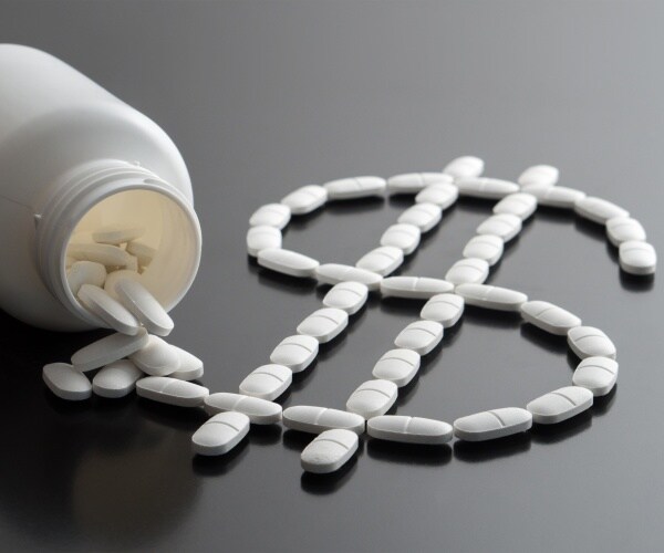 pills spilling out of bottle in shape of a dollar sign