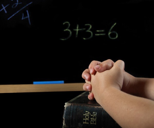 a childs hands folded in prayer with a bible and blackboard with math problems in the background