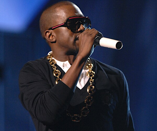 kanye west holds a mic tight to his face while speaking to a crowd