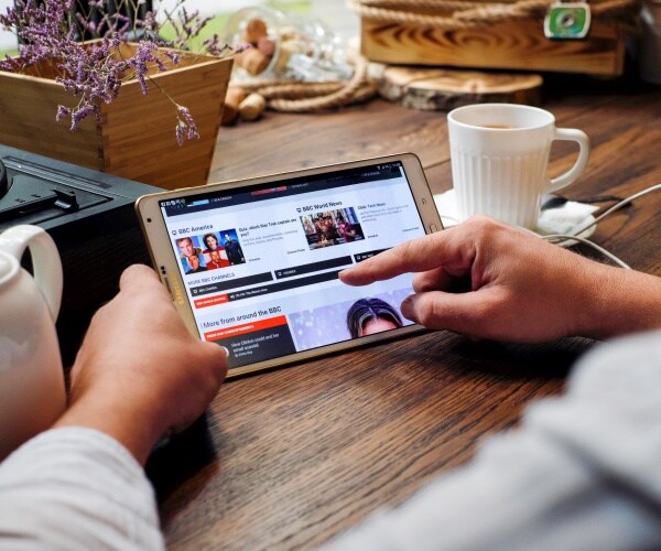person using a tablet to scroll through the news with a cup of coffee nearby