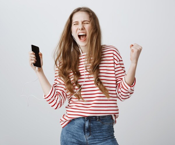 young woman listening to music on her smartphone with earbuds, singing and dancing