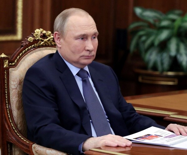 vladimir putin sits at a desk