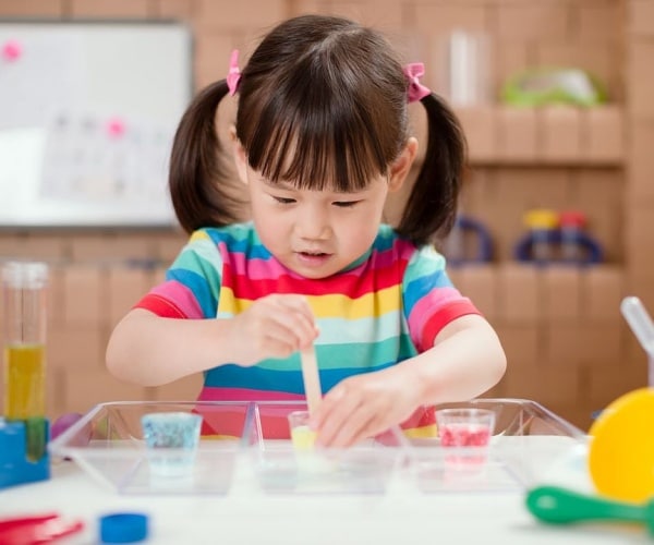young girl wearing a striped shirt of many colors doing an experiment at a table