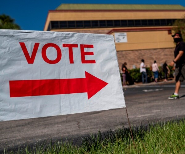 white sign with "vote" in red letters with people walking by