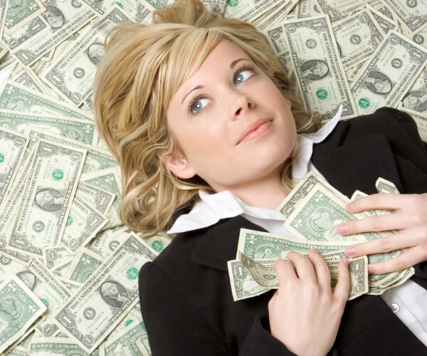 a happy woman lying on a pile of one dollar bills