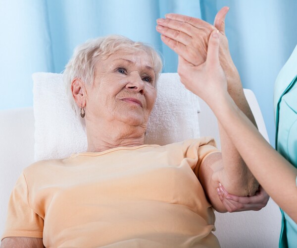 an elderly woman with her arm raised during rehab