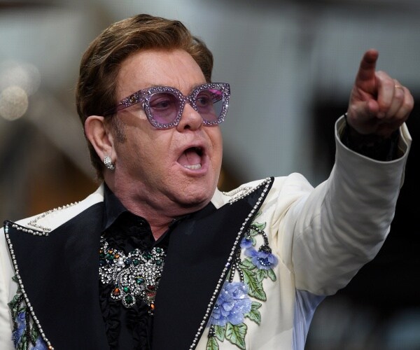 elton john in a white blazer with blue floral print and purple sunglasses