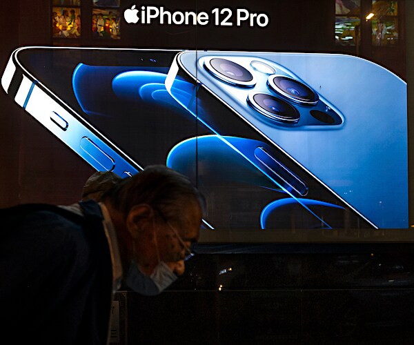 an apple iphone 12 ad on a store front as a masked man walks by