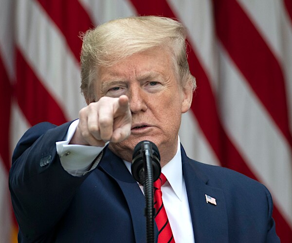 president donald trump in front of an american flag points straight ahead