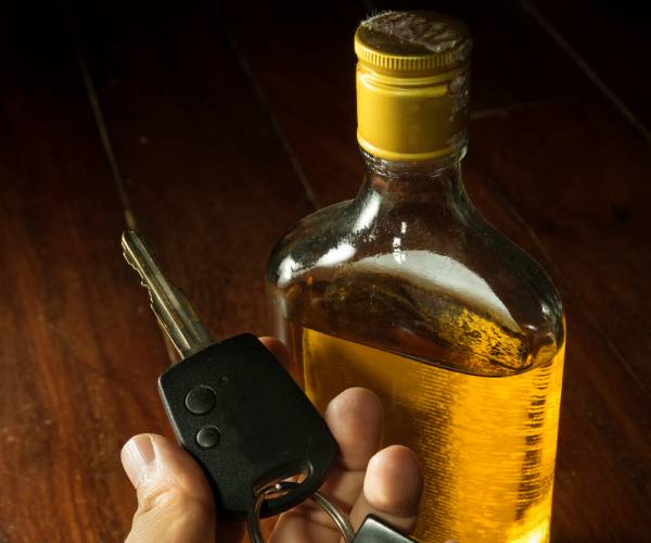 a bottle of liquor and a hand holding car keys