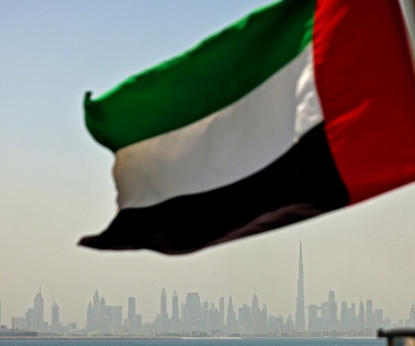 emirati flag sways in the wind as the skyline of dubai is seen in the background